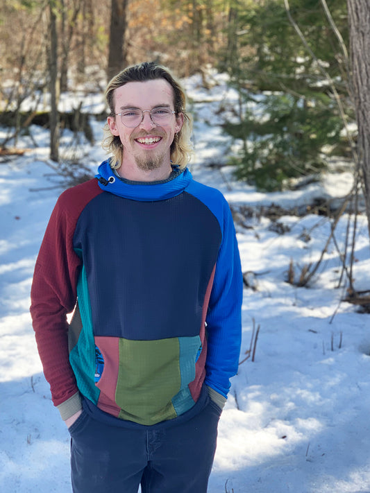 A male model wears a multicolor, unique, one of a kind, patchwork one-off Thuja Burrow fleece hoodie in the snow..